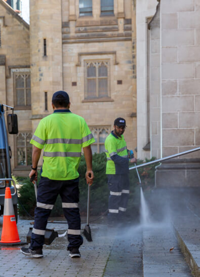 Commercial cleaning team carrying out high pressure cleaning of dirty exterior of office building